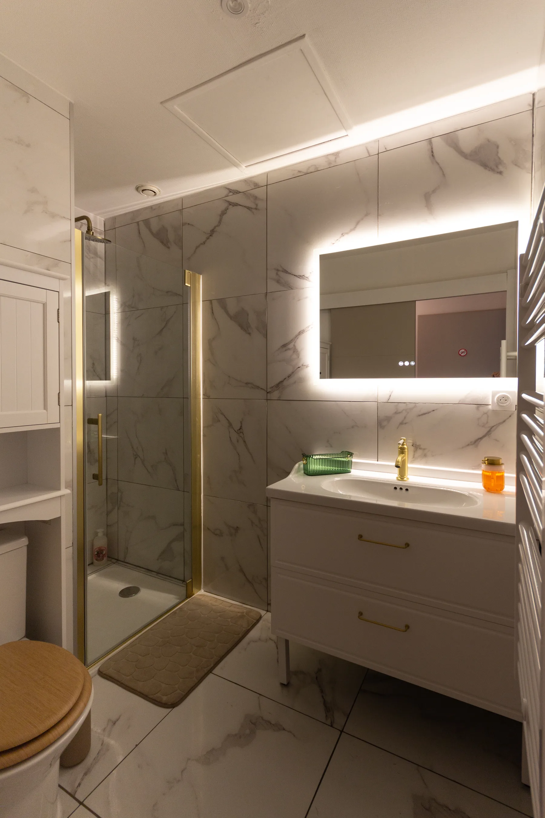 Salle d'eau après rénovation avec douche vitrée, carrelage effet marbre et meuble vasque lumineux